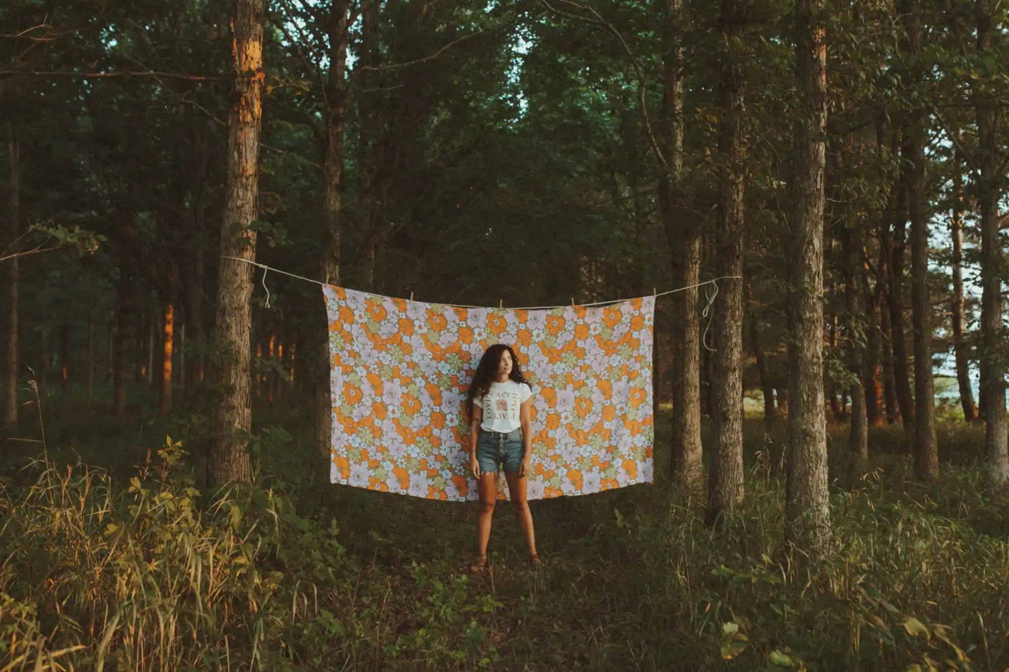 A young woman standing in front of a patterned blanket hung on a clothesline between trees.